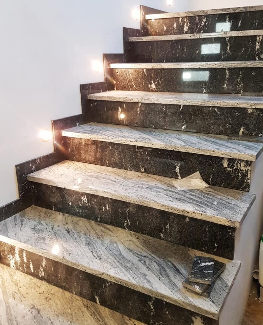 Wykończone kamienne schody wewnętrzne w Cycowie z podświetleniem punktowym. Na dolnym stopniu leżą próbki kamienia w ciemnym kolorze.