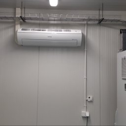 FRIGOPARTNER Bogdan Kobyliński - Wewnętrzna jednostka klimatyzacji Samsung zamontowana na panelowej ścianie w pomieszczeniu technicznym, widoczne koryta kablowe pod sufitem i szafa sterownicza z kratkami wentylacyjnymi.