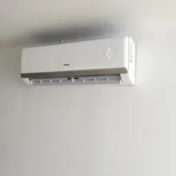 Biała klimatyzacja marki Gree zamontowana na jasnej ścianie, wyświetlająca temperaturę 21 stopni Celsjusza.