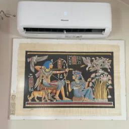 Biały klimatyzator Hisense nad egipskim papirusem z faraonami i zwierzętami. Nowoczesność i starożytność w jednym kadrze.