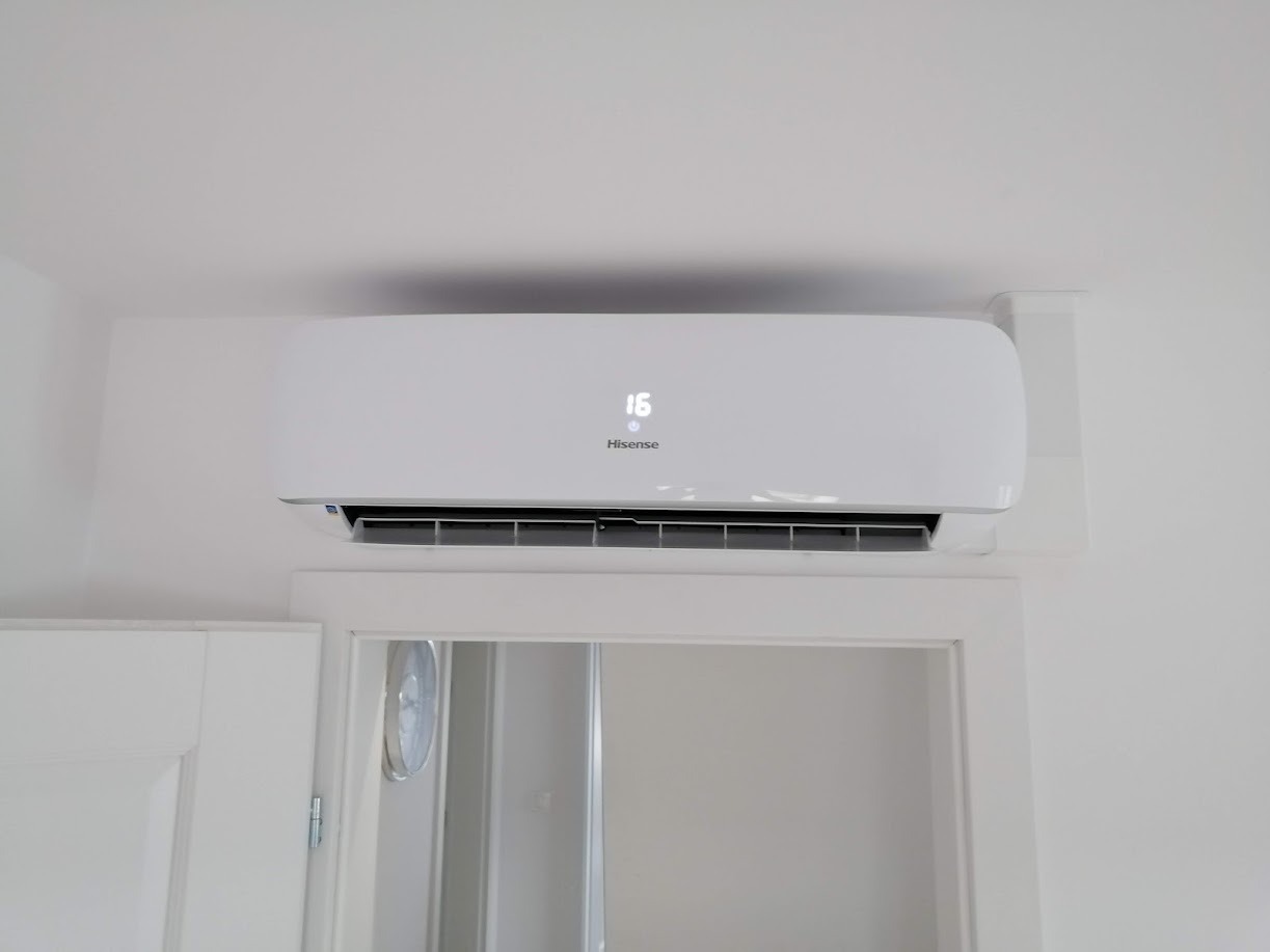 Biała klimatyzacja Hisense zamontowana nad drzwiami, wyświetlająca temperaturę 16 stopni Celsjusza, widoczna z dołu.
