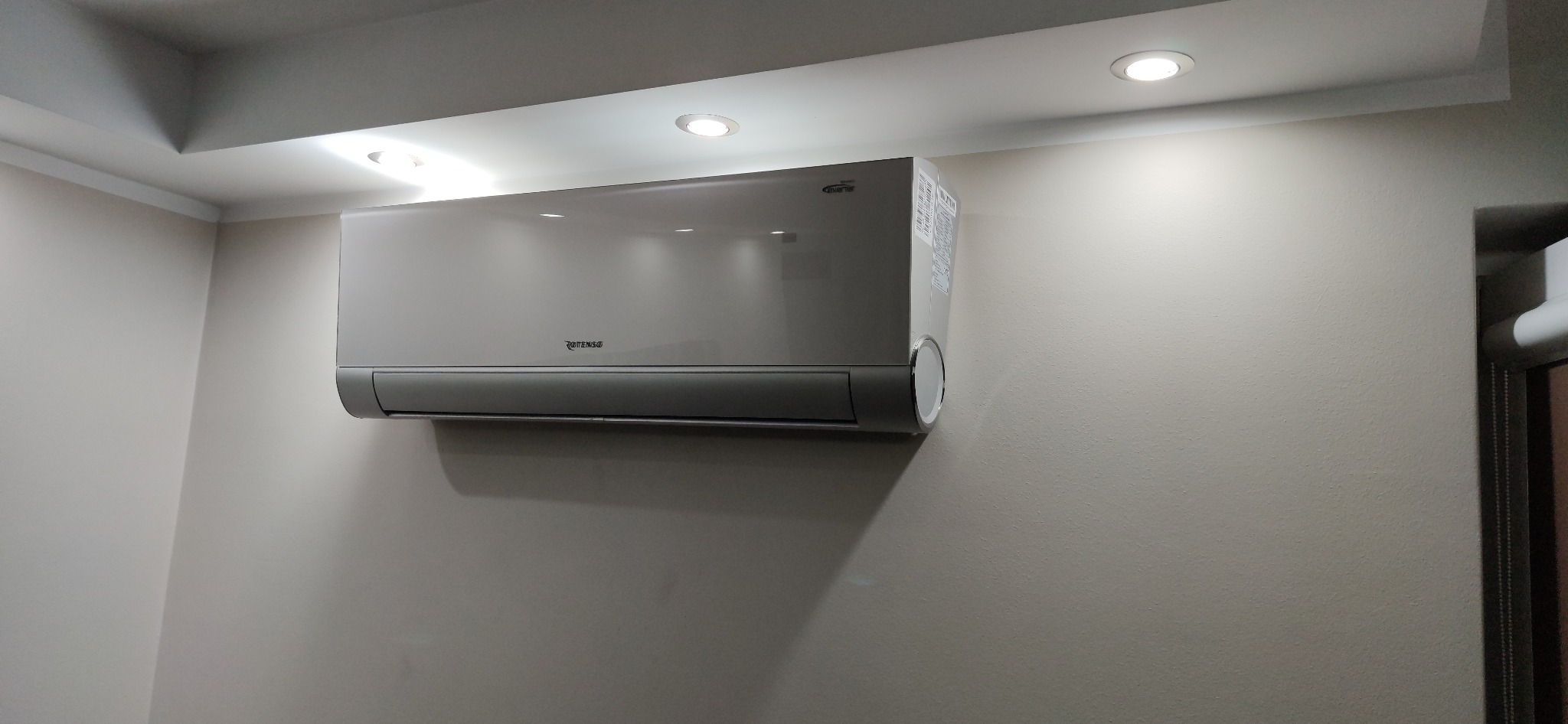 Biała jednostka klimatyzacji Rotenso zamontowana na ścianie w jasnym pomieszczeniu z oświetleniem sufitowym.