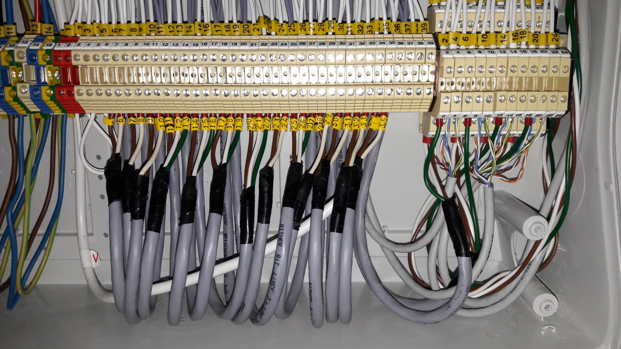 Panel elektryczny z podłączonymi przewodami, widoczne złącza śrubowe i oznaczenia numerów na przewodach.