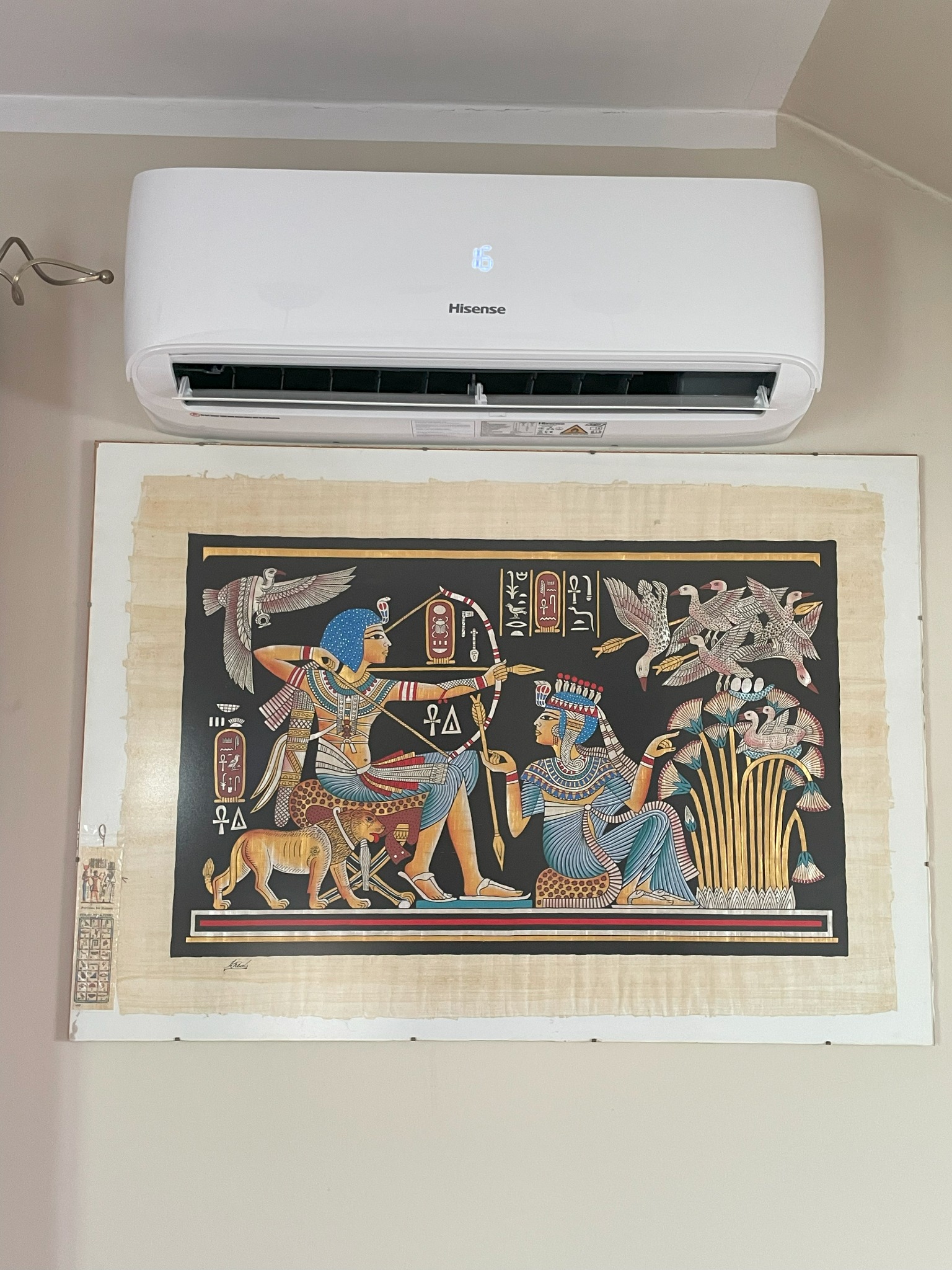 Biały klimatyzator Hisense nad egipskim papirusem z faraonami i zwierzętami. Nowoczesność i starożytność w jednym kadrze.