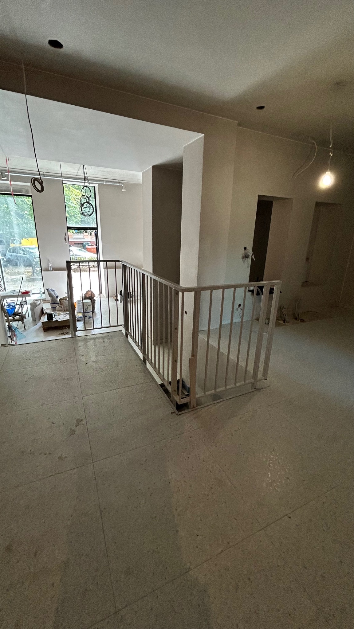 Wnętrze w trakcie wykańczania z zamontowaną metalową balustradą schodową o prostej konstrukcji. Widoczne okna i elementy instalacji elektrycznej.