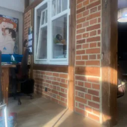 Fragment odnowionego wnętrza w Świebodzinie z ceglaną ścianą i drewnianymi belkami, widoczne biurko i krzesło, na ścianie obraz i kalendarz.