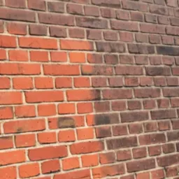 Częściowo oczyszczona ceglana ściana zewnętrzna, kontrast między jasnoczerwoną, odnowioną powierzchnią a ciemniejszym, zabrudzonym fragmentem.