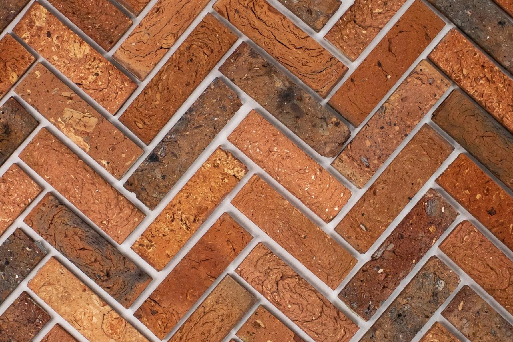 Ułożona w jodełkę okładzina z cegieł klinkierowych w odcieniach czerwieni i brązu, z widoczną fakturą i jasnymi fugami.