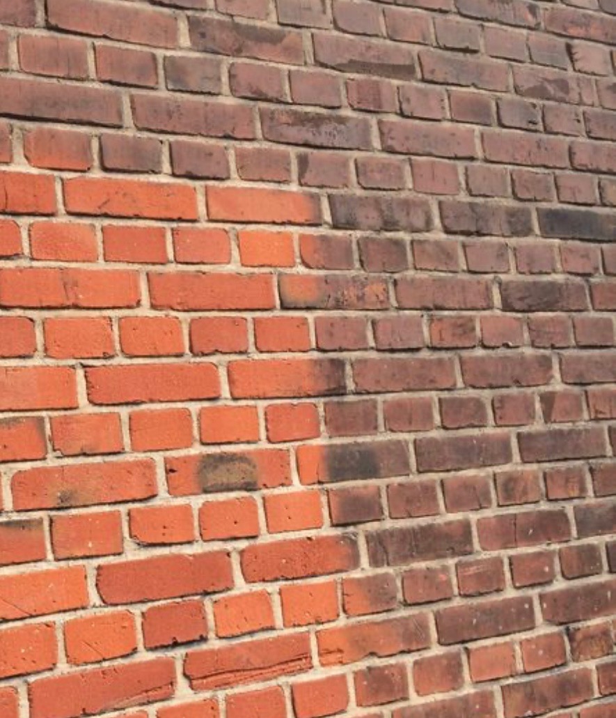 Częściowo oczyszczona ceglana ściana zewnętrzna, kontrast między jasnoczerwoną, odnowioną powierzchnią a ciemniejszym, zabrudzonym fragmentem.