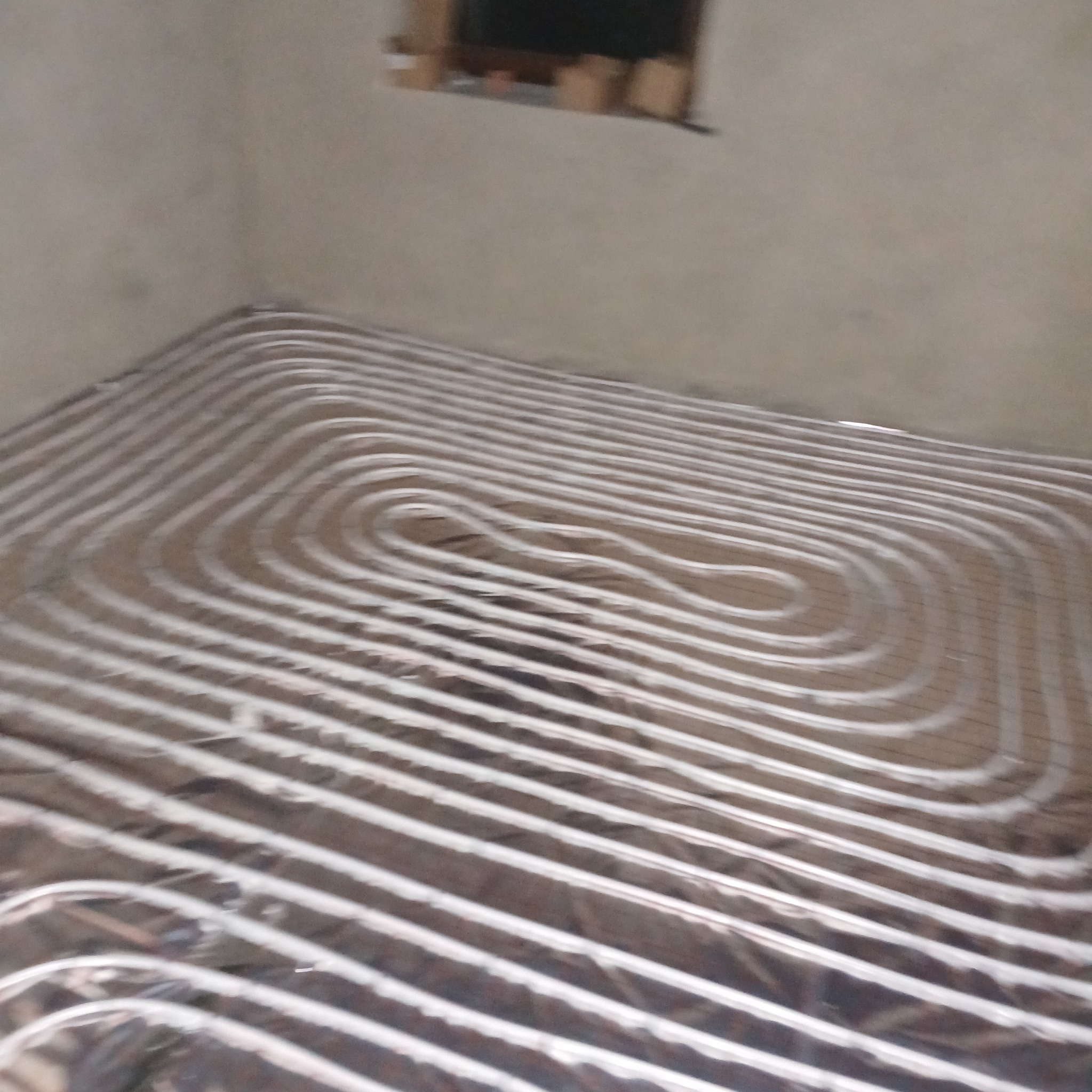 Rury ogrzewania podłogowego ułożone w pętle na folii izolacyjnej w surowym pomieszczeniu, przygotowane do zalania wylewką.