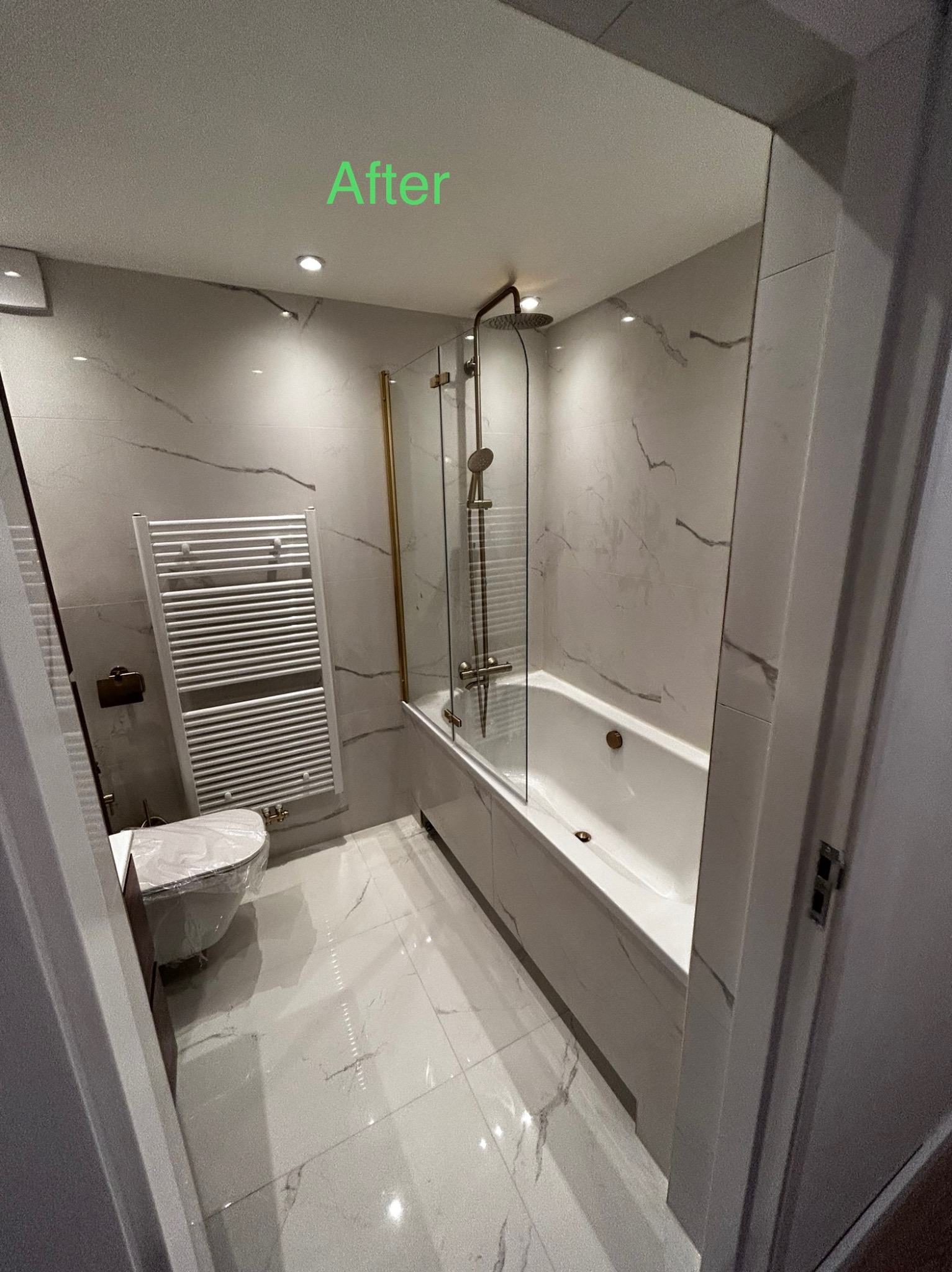 Wykończona łazienka po remoncie z wanną z parawanem nawannowym w złotym kolorze, grzejnikiem drabinkowym i toaletą jeszcze w folii ochronnej.