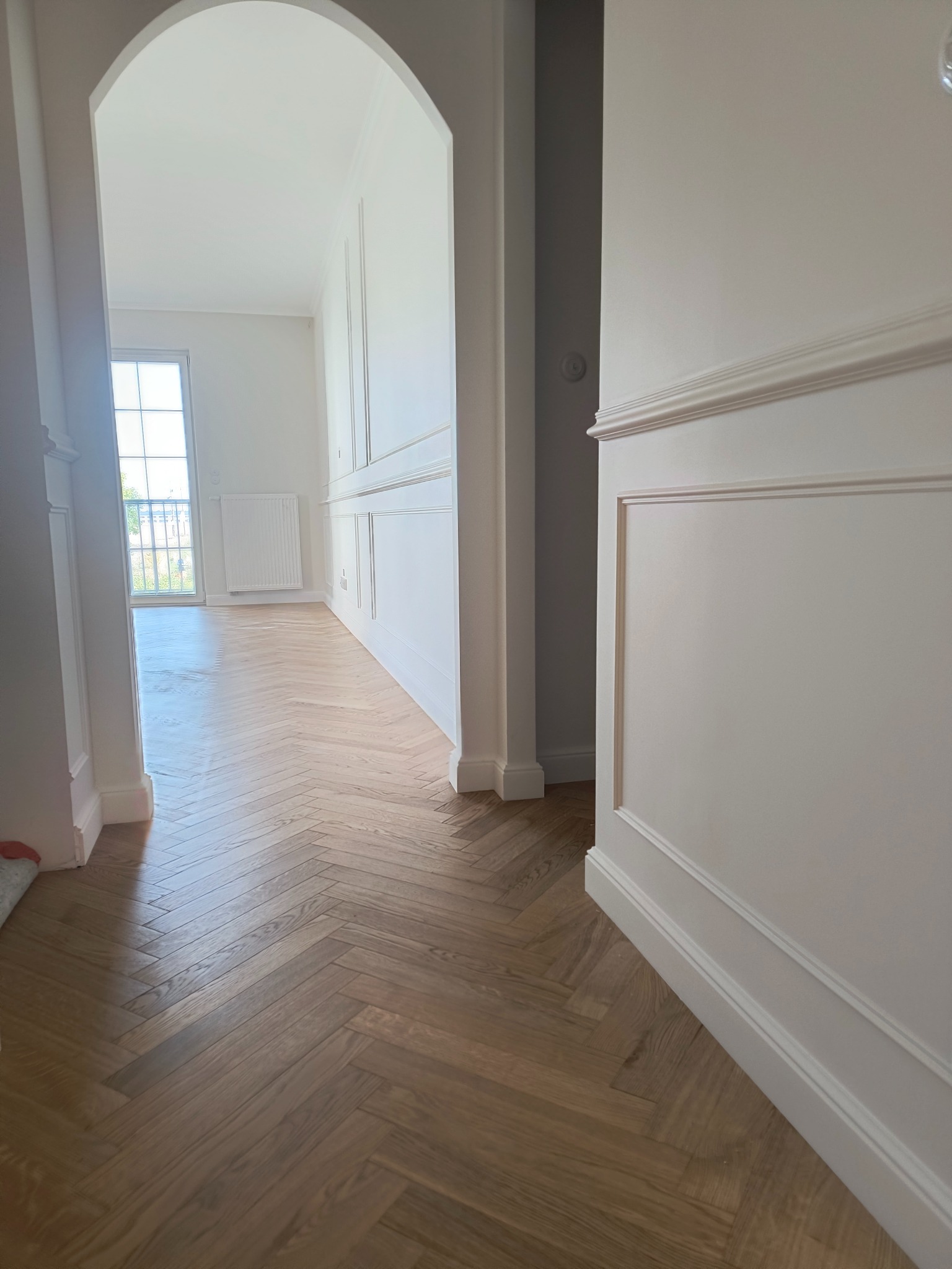 Parkiet ułożony we wzór jodełki francuskiej w korytarzu z białymi ścianami i dekoracyjnymi listwami.