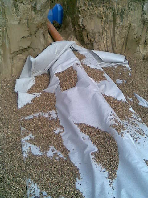 Instalacja drenażu rozsączającego oczyszczalni ścieków IN-DRAN w wykopie, widoczna rura drenażowa, geowłóknina i warstwa żwiru.