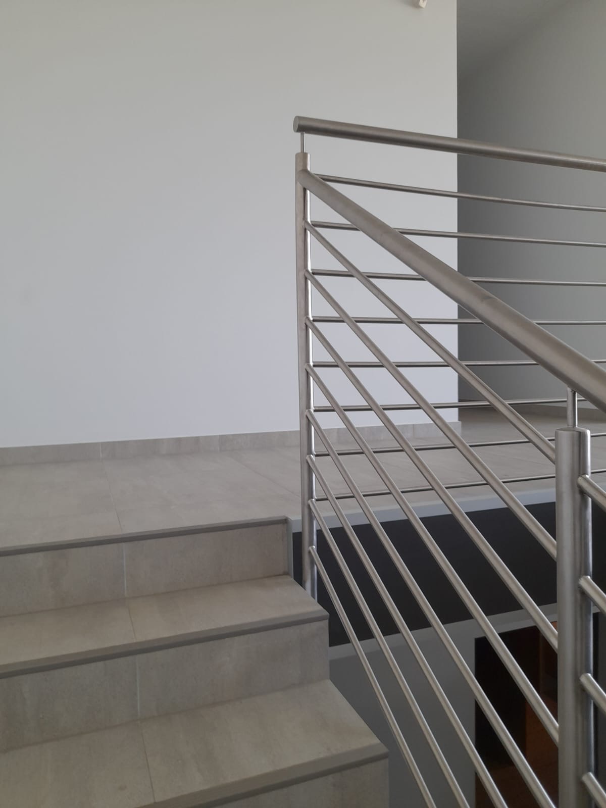 Nowoczesna balustrada ze stali nierdzewnej z poziomymi wypełnieniami zamontowana przy schodach wyłożonych płytkami w jasnych odcieniach szarości.