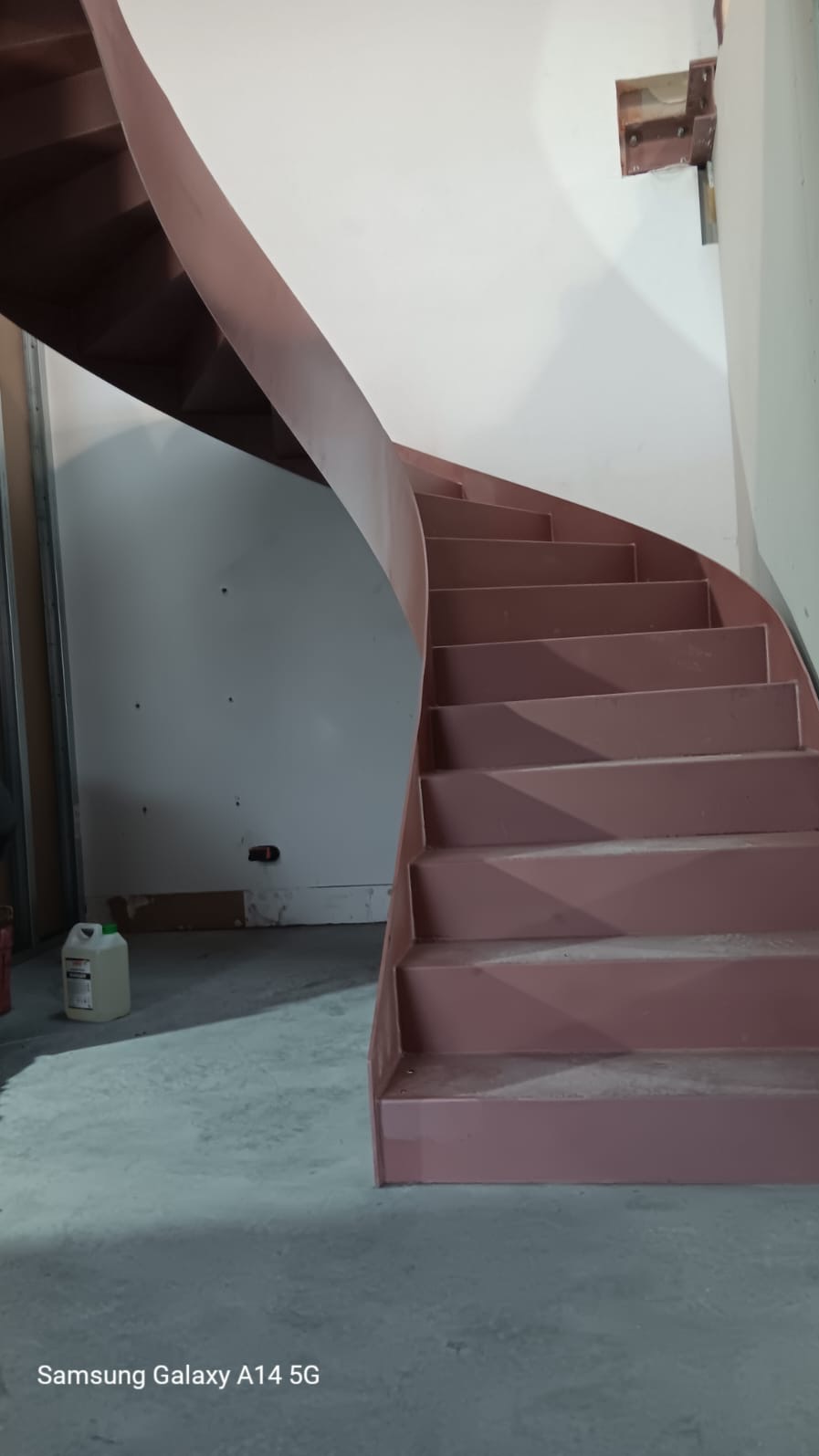 Metalowe schody spiralne w trakcie montażu, widoczne mocowania do ściany, surowy stan wykończenia wnętrza.