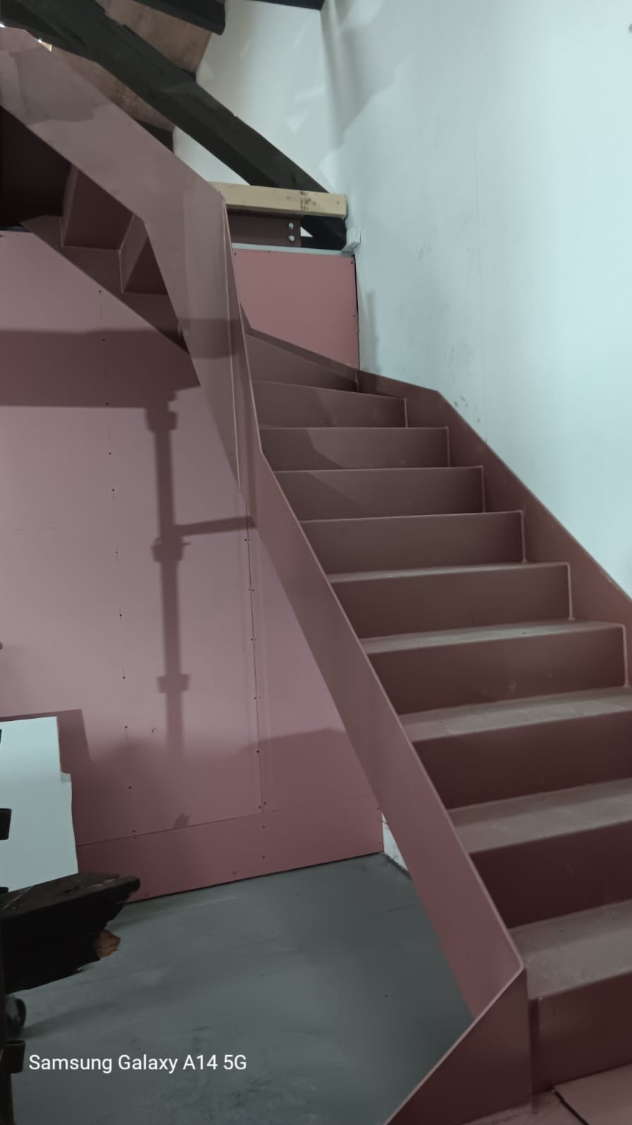 Konstrukcja schodów wewnętrznych z metalu, z surowym wykończeniem, widoczne elementy montażowe i płyty gipsowo-kartonowe na ścianach.