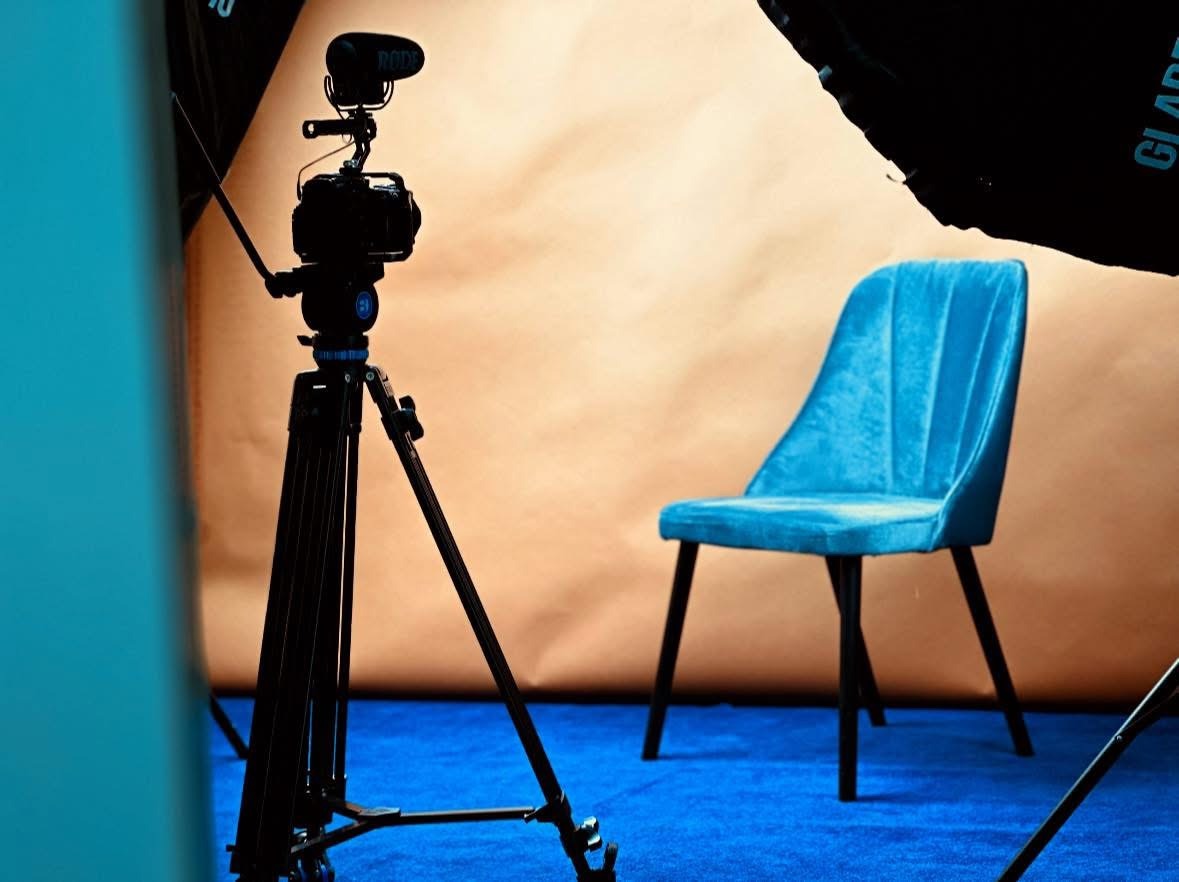 Profesjonalne studio fotograficzne z kamerą na statywie, oświetleniem i turkusowym krzesłem na niebieskim tle, gotowe do sesji zdjęciowej.