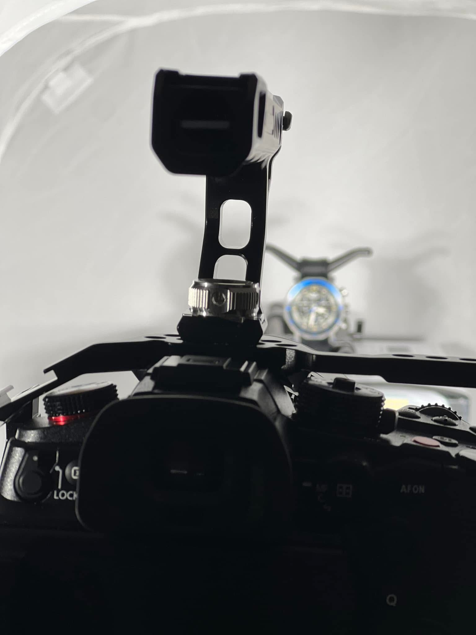 Czarny aparat z mikrofonem i lampą błyskową w tle, ustawiony w studiu fotograficznym. Widoczne detale mocowania i ustawienia sprzętu.