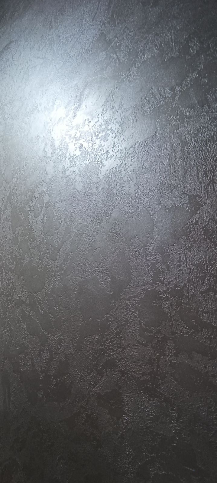 Tekstura ściany w odcieniach szarości z efektem dekoracyjnego tynku, delikatnie odbijająca światło.