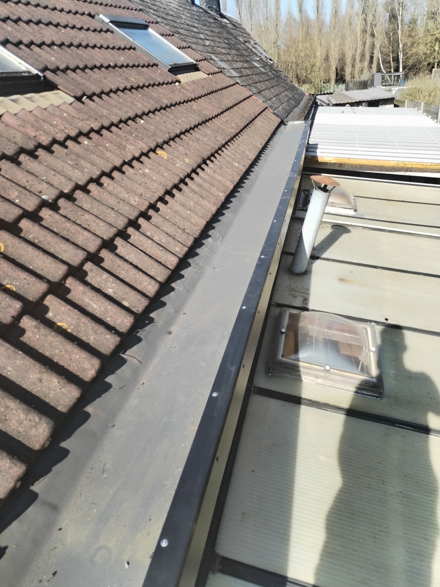 Nowy, metalowy system rynnowy zamontowany na dachu z dachówką ceramiczną, widoczny kominek wentylacyjny i świetlik dachowy