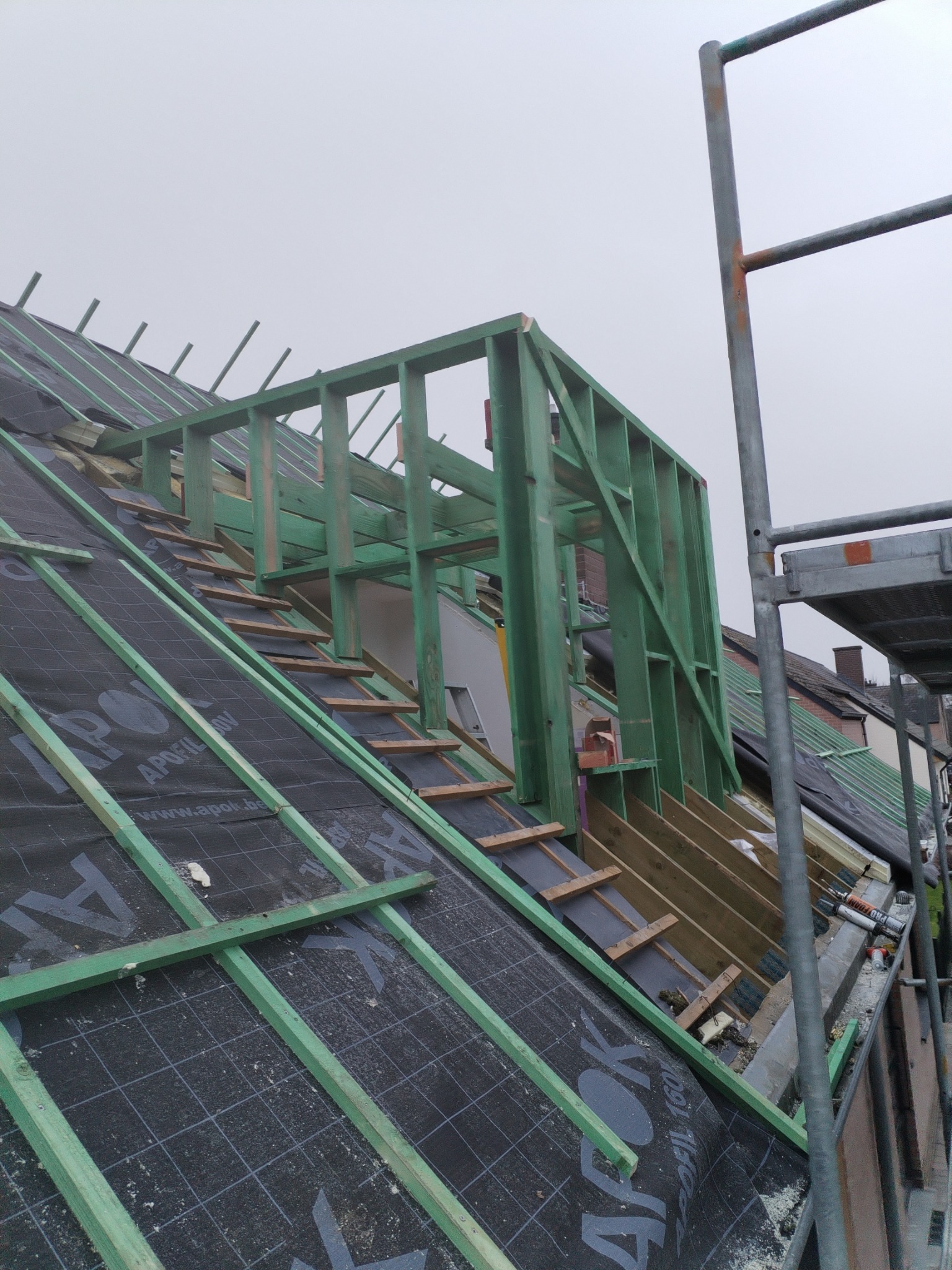 Konstrukcja drewniana lukarny w trakcie budowy na dachu pokrytym membraną w Człuchowie, widoczne rusztowanie i drabina dekarska.