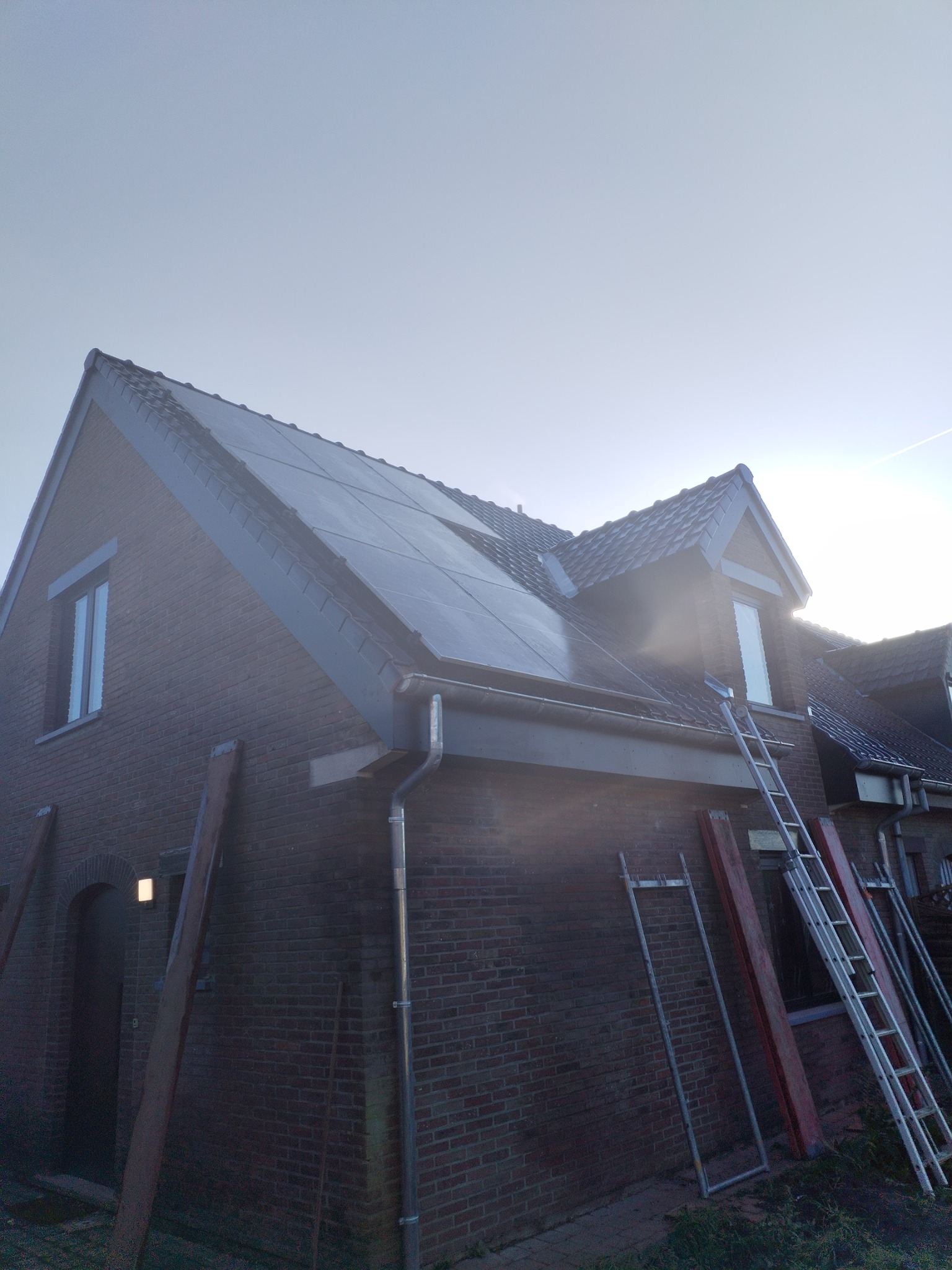 Dom z cegły z nowymi panelami słonecznymi na dachu, widoczne drabiny i rusztowania.