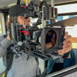 Operator z profesjonalną kamerą RED Digital Cinema z zamontowanymi akcesoriami SmallHD i Tilta, w trakcie filmowania, widoczny kadr z odbiciem w obiektywie.