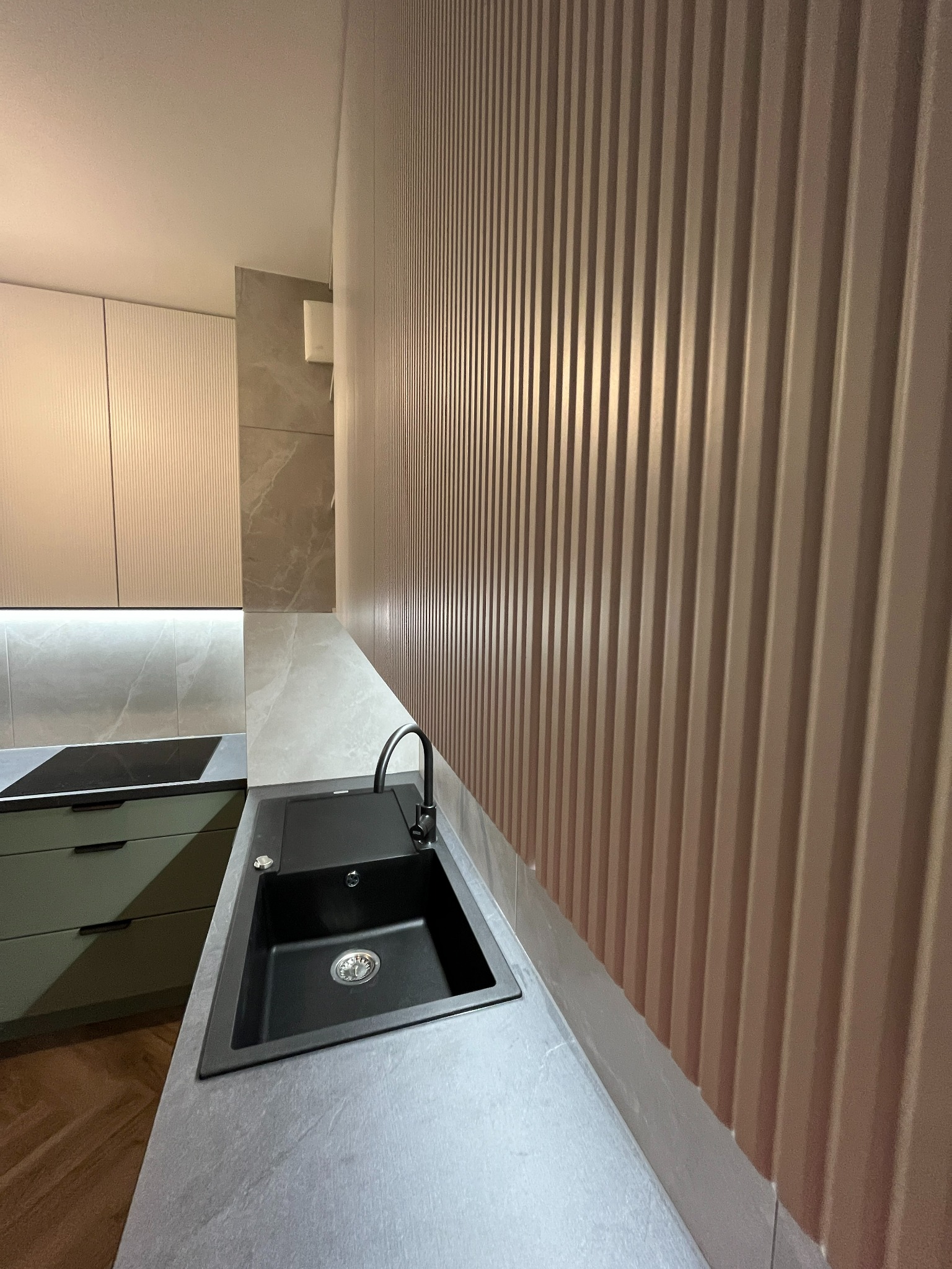 Nowoczesna kuchnia: czarny zlew wpuszczony w szary blat, minimalistyczne szafki z ryflowanymi frontami i dekoracyjna ściana z pionowymi panelami.