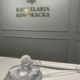 Kryształowy młotek sędziowski na marmurowym biurku, w tle napis Kancelaria Adwokacka na ścianie.