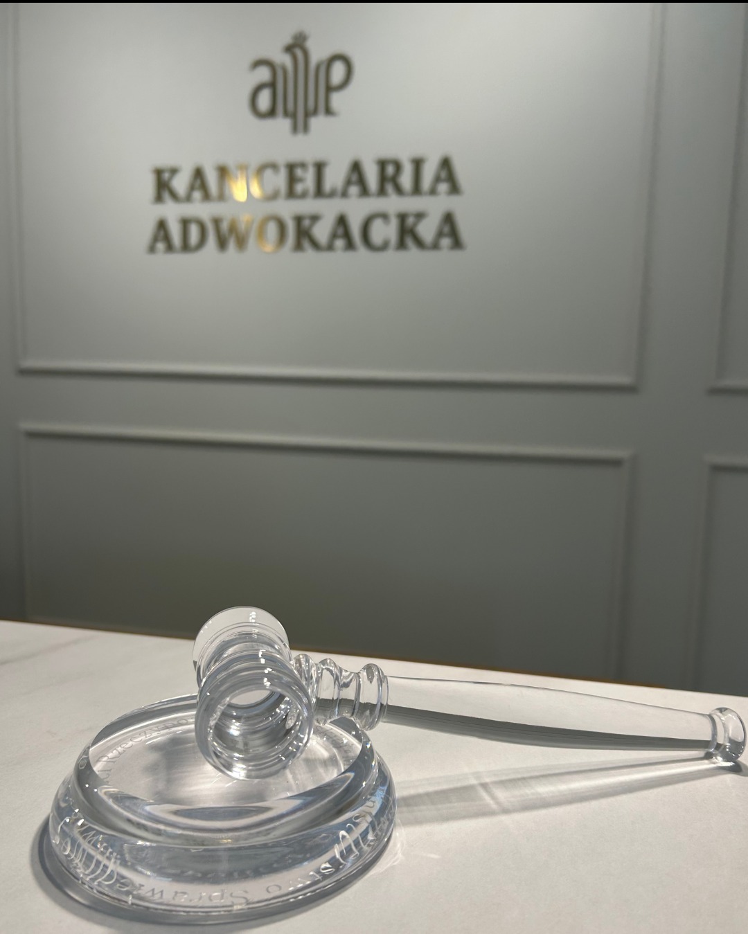 Kryształowy młotek sędziowski na marmurowym biurku, w tle napis Kancelaria Adwokacka na ścianie.