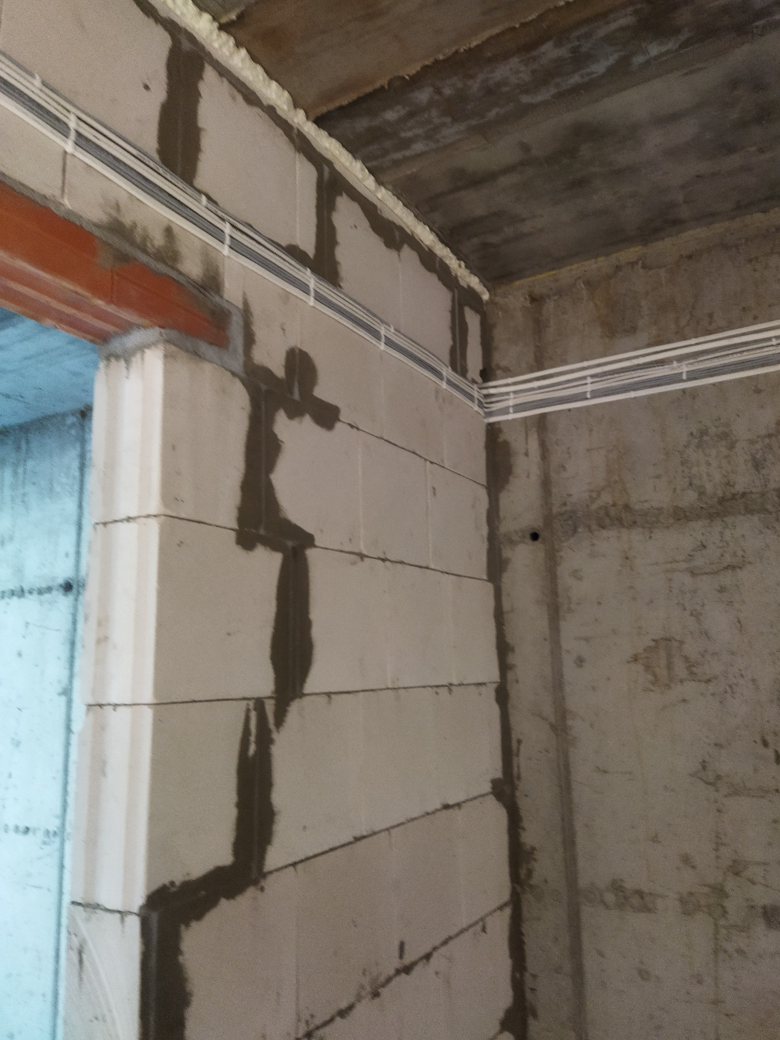 Surowe wnętrze w trakcie budowy: ściany z betonu komórkowego z poprowadzonymi białymi przewodami elektrycznymi, zaprawa między blokami, surowy betonowy sufit.