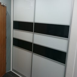 BUMEB RAFAŁ GUSTOŁEK - Nowoczesna szafa wnękowa z przesuwnymi drzwiami, biało-czarne poziome pasy, srebrne ramy, widoczna część podłogi z ciemnych płytek.