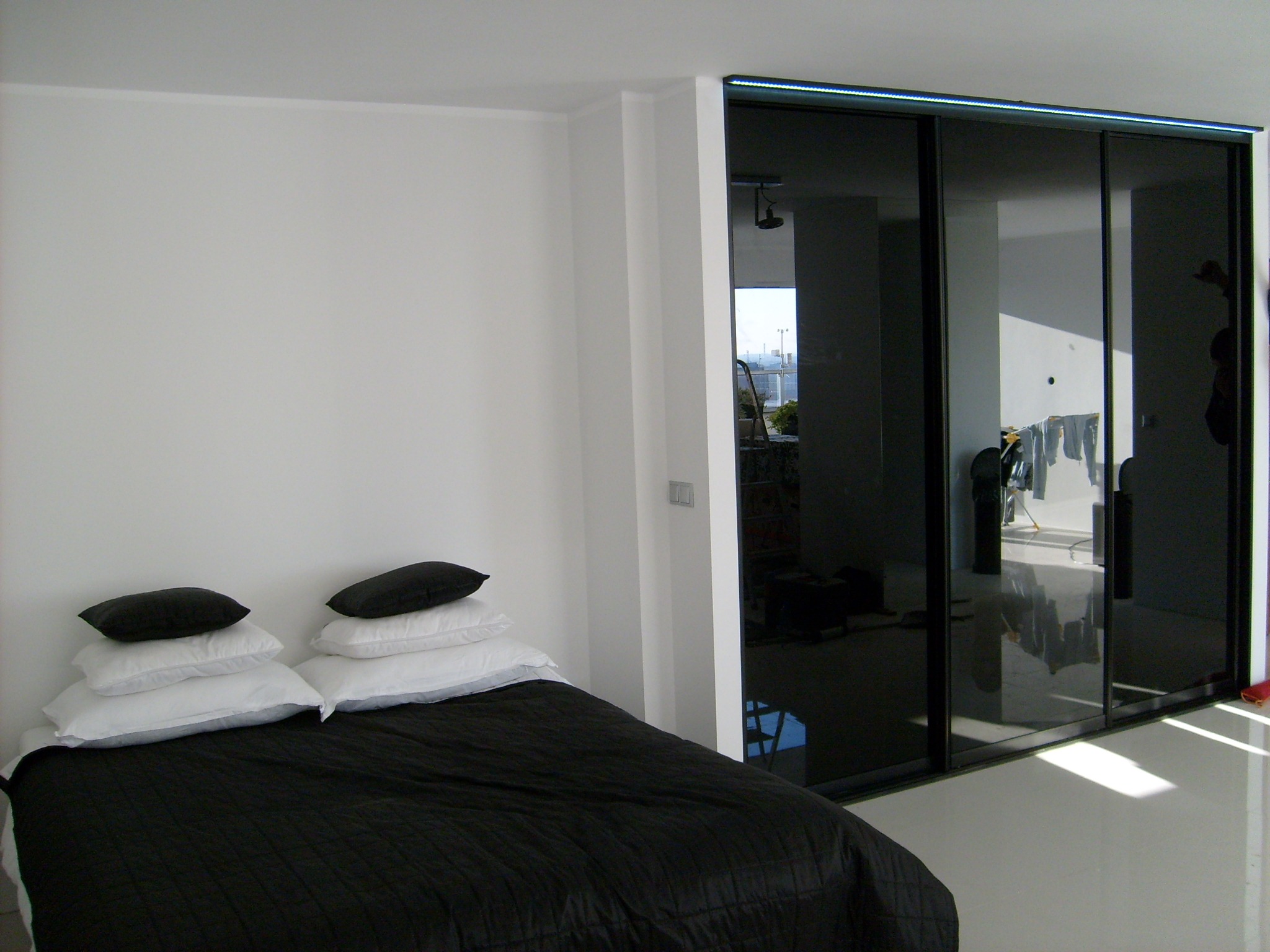 Nowoczesna sypialnia z czarno-białą pościelą i dużą szafą przesuwną z czarnymi szklanymi drzwiami, odbijającymi widok z balkonu.