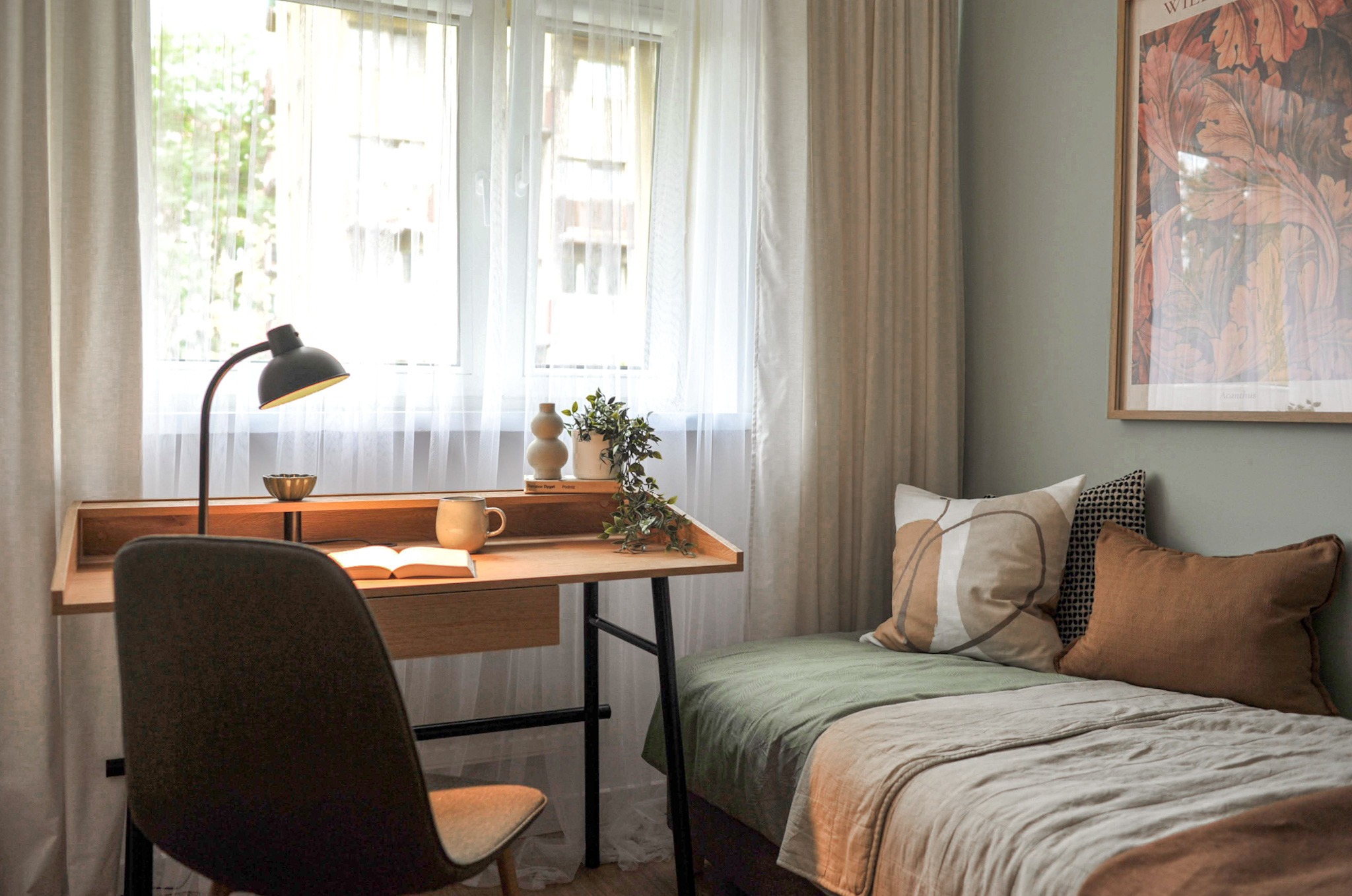Pokój z biurkiem przy oknie, łóżkiem z dekoracyjnymi poduszkami i plakatem na ścianie, utrzymany w stonowanej kolorystyce.