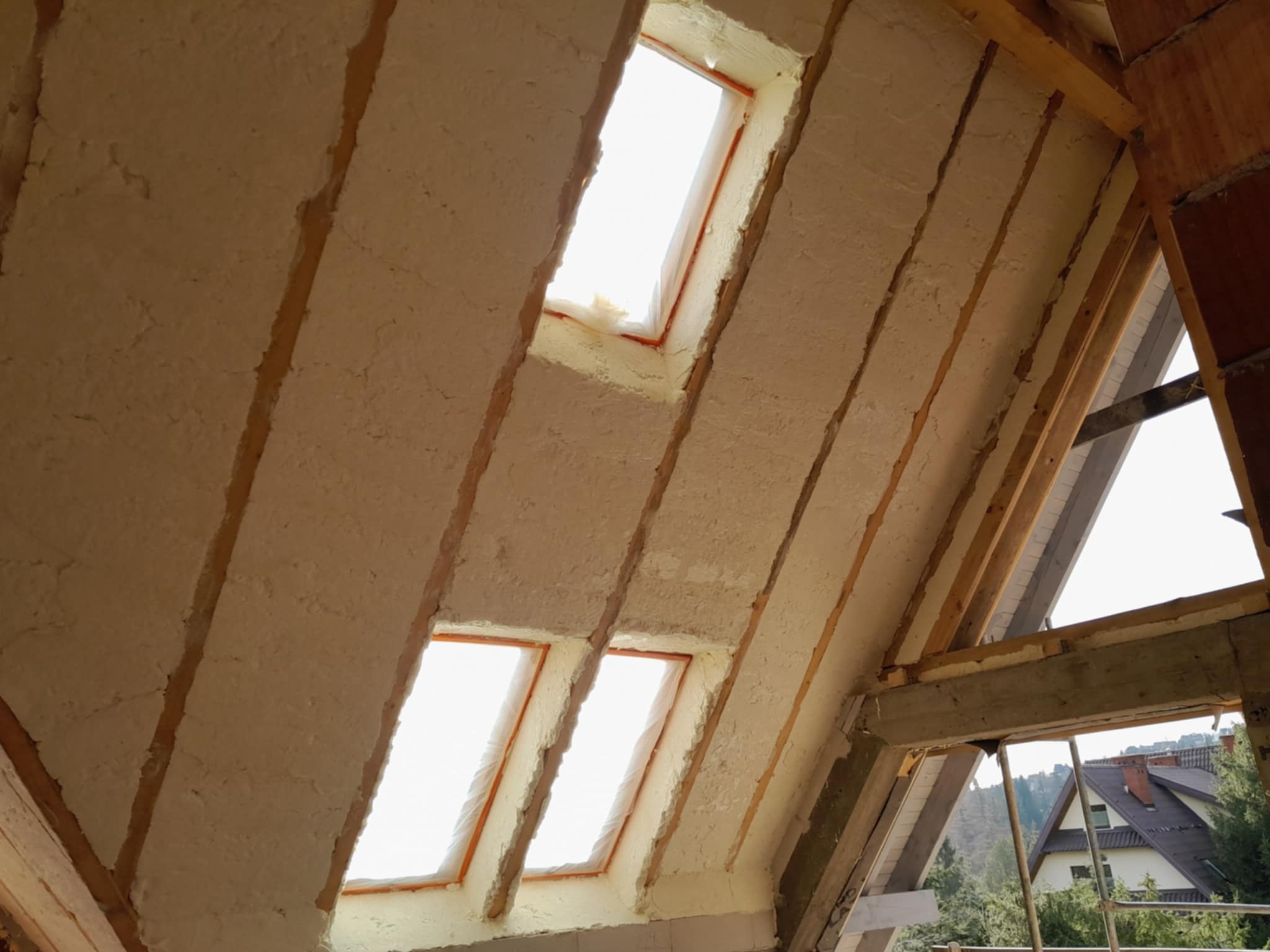 Poddasze z oknami dachowymi po ociepleniu pianką PUR, widoczne krokwie i fragment konstrukcji więźby dachowej, jasne światło wpadające przez okna.