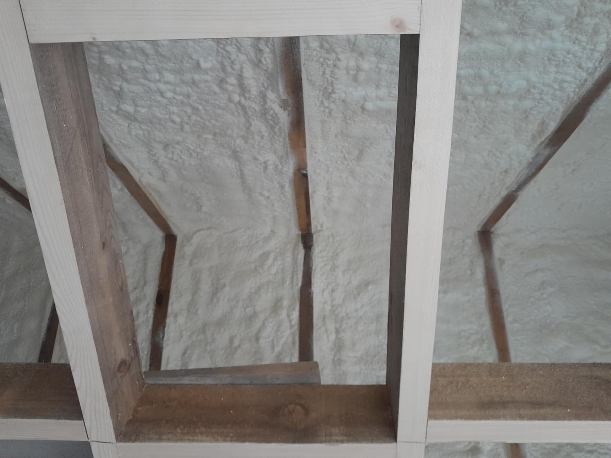 Poddasze z drewnianą konstrukcją krokwiową wypełnione szarobiałą pianką izolacyjną o nieregularnej strukturze