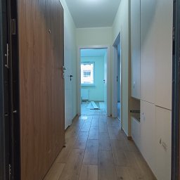 ExpressRemont - Wnętrze korytarza po remoncie z drewnopodobnymi płytkami na podłodze, zabudową szafy wnękowej po prawej stronie i widokiem na dalsze pomieszczenia.