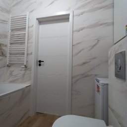 ExpressRemont - Nowoczesna łazienka z marmurowymi płytkami na ścianach, drewnopodobną podłogą, białą armaturą i grzejnikiem drabinkowym.
