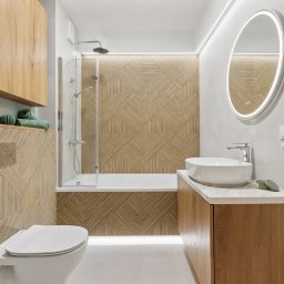 ExpressRemont - Nowoczesna łazienka z drewnianymi akcentami: geometryczne płytki, owalne lustro z podświetleniem LED, biała umywalka nablatowa i grzejnik drabinkowy.
