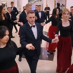 Czaro Filmuje - Cezary Cichowski - Uczestnicy studniówki w trakcie poloneza. Młodzież w strojach wieczorowych, dziewczęta w bordowych spódnicach i czarnych bluzkach, chłopcy w garniturach z muszkami.