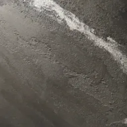 Ciemna, szpachlowana ściana z widoczną, jaśniejszą smugą świeżo nałożonej masy, ukazująca nierównomierną strukturę i fakturę powierzchni.