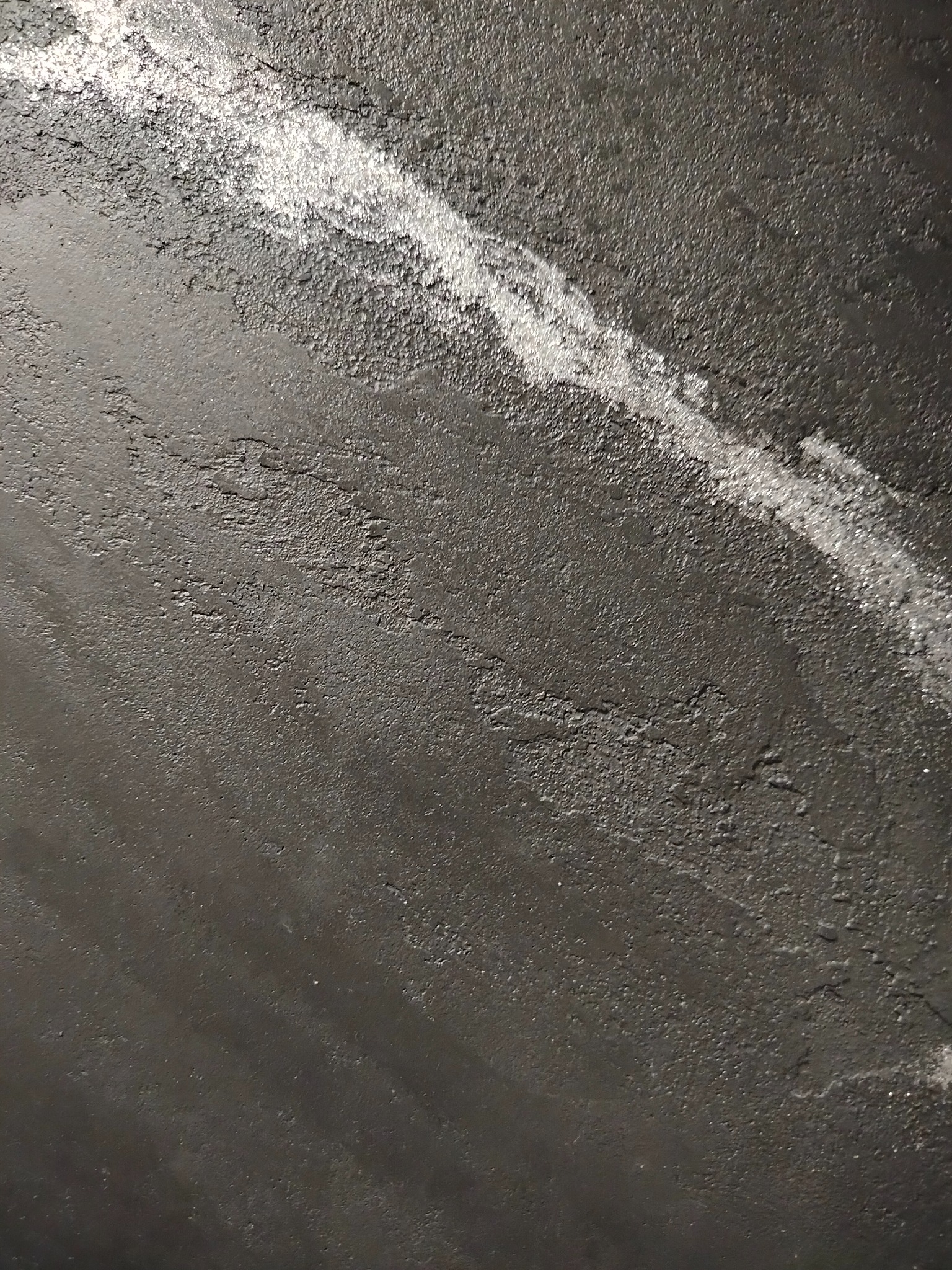 Ciemna, szpachlowana ściana z widoczną, jaśniejszą smugą świeżo nałożonej masy, ukazująca nierównomierną strukturę i fakturę powierzchni.