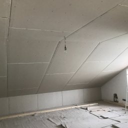 Rewall - Poddasze z zamontowanymi płytami kartonowo-gipsowymi na skosach i ścianach. Widoczna drabina, surowe wykończenie, przygotowanie do dalszych prac.