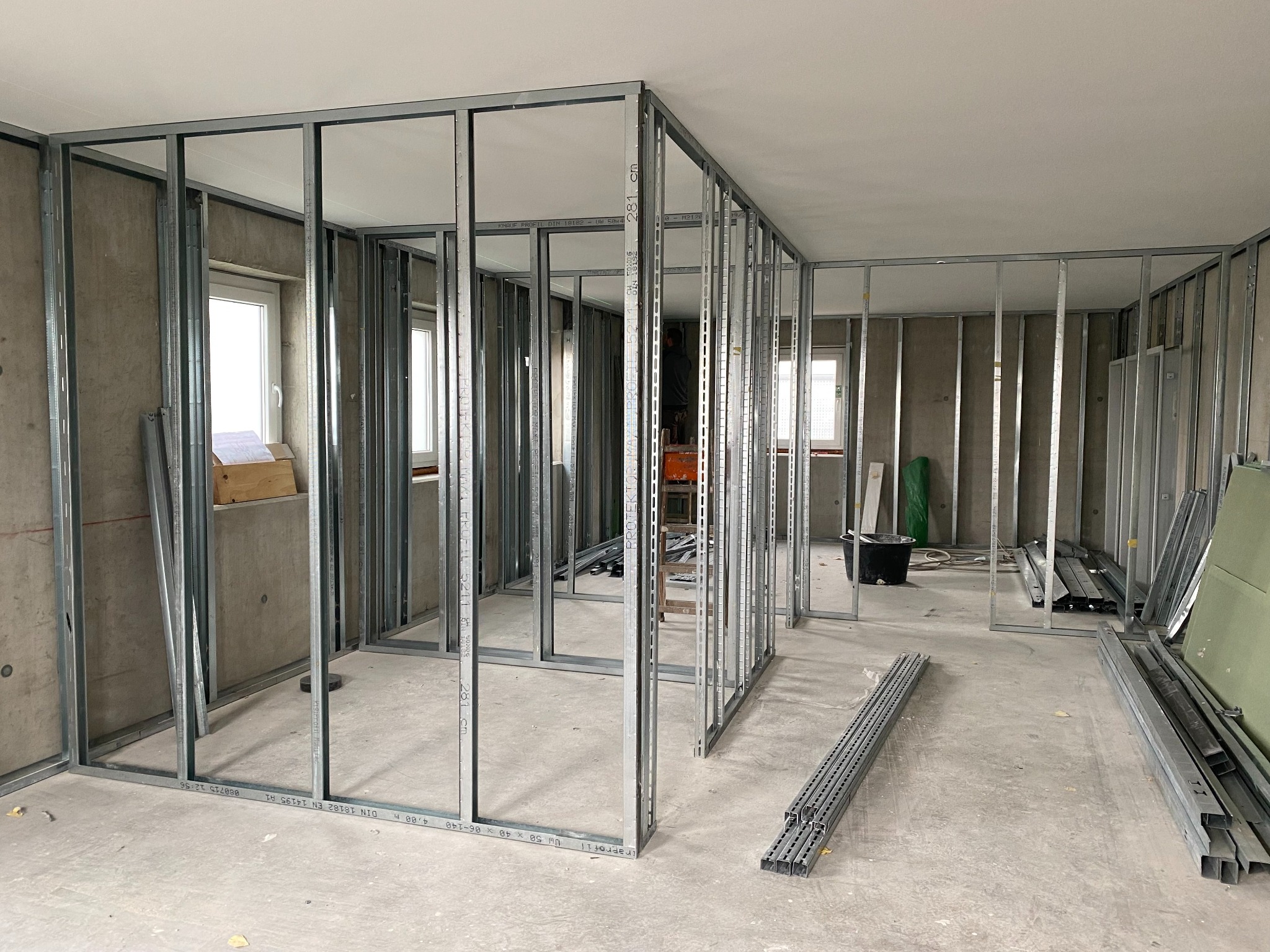 Konstrukcja szkieletowa z profili stalowych w surowym wnętrzu, przygotowana pod montaż płyt kartonowo-gipsowych. Widoczne okna i elementy instalacji.