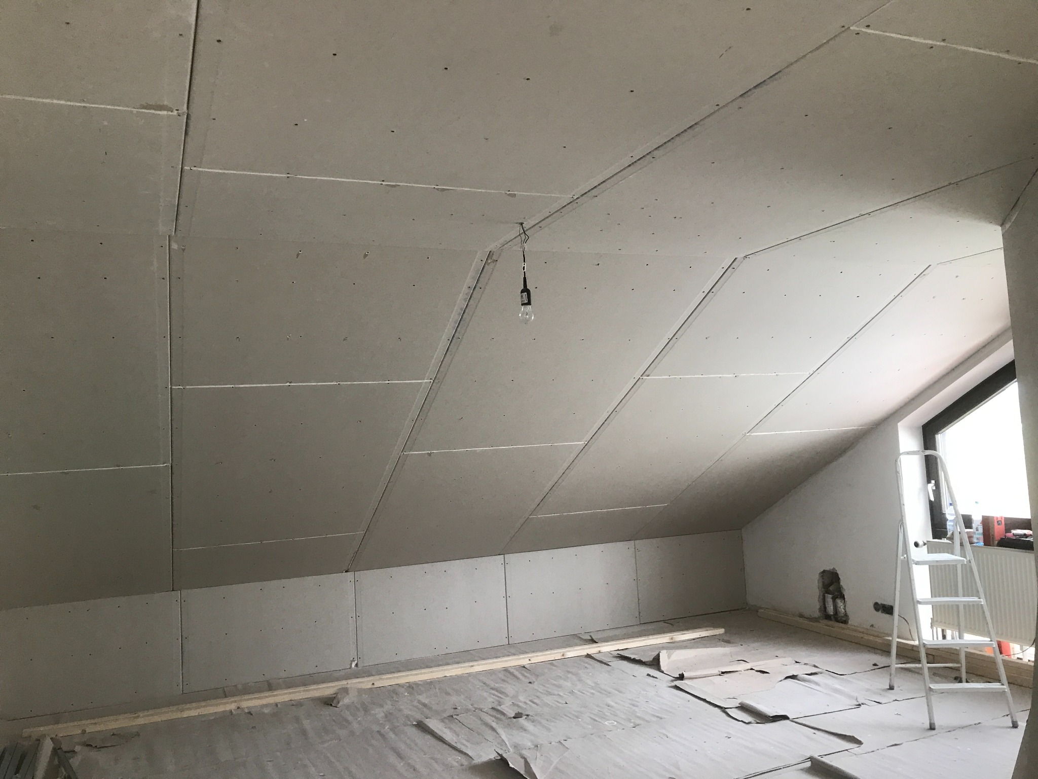 Poddasze z zamontowanymi płytami kartonowo-gipsowymi na skosach i ścianach. Widoczna drabina, surowe wykończenie, przygotowanie do dalszych prac.