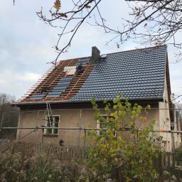 Dach Marzeń Michał DWORACZEK - Dom jednorodzinny w trakcie krycia dachu blachodachówką modułową; widoczne łaty, częściowo ułożone panele, komin z cegły, rusztowanie i pracujący dekarz.