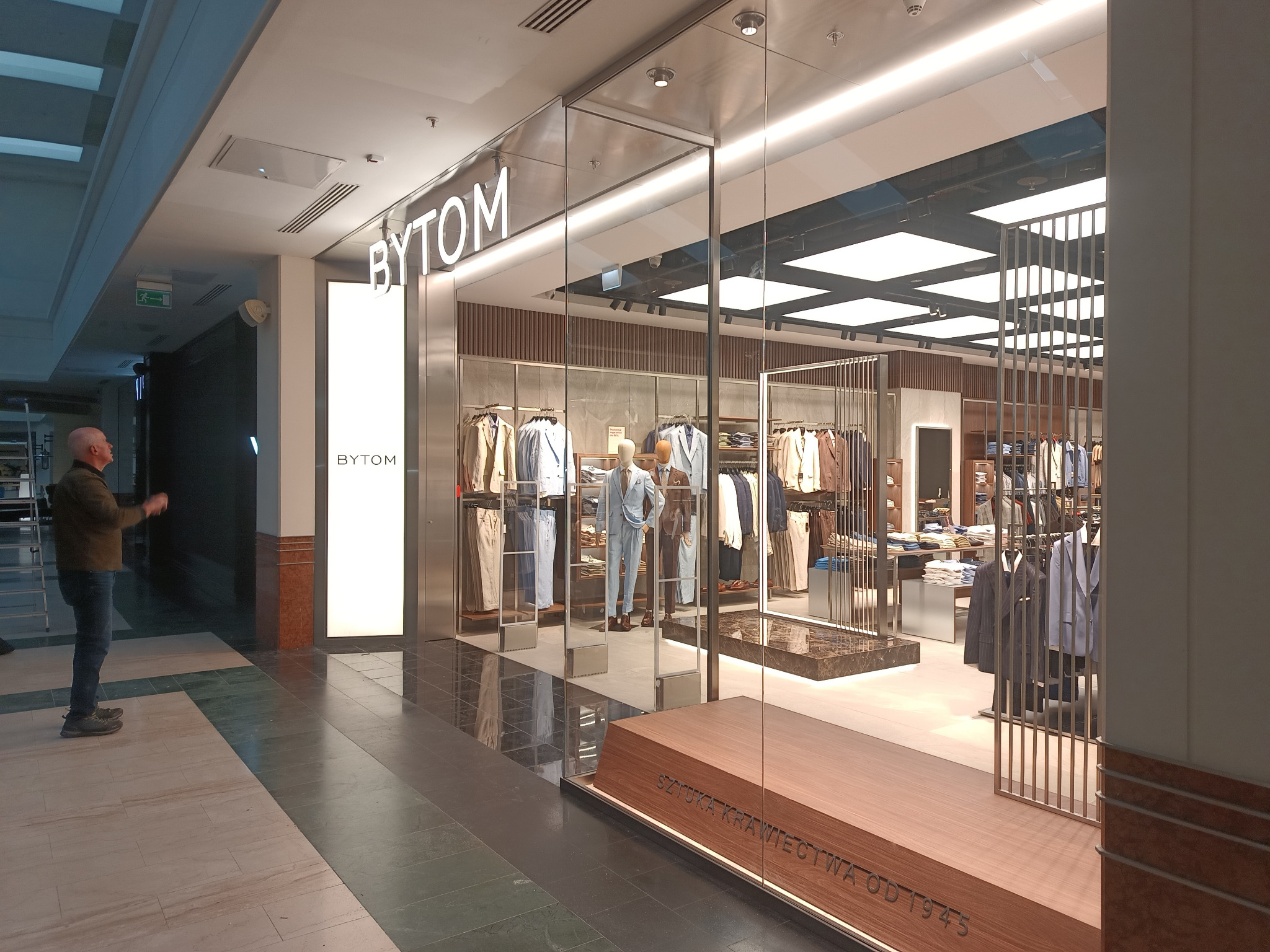 Elegancka witryna sklepu odzieżowego Bytom, obłożona szlifowaną blachą ze stali nierdzewnej AISI304. Widoczny fragment wnętrza sklepu i sylwetka mężczyzny.