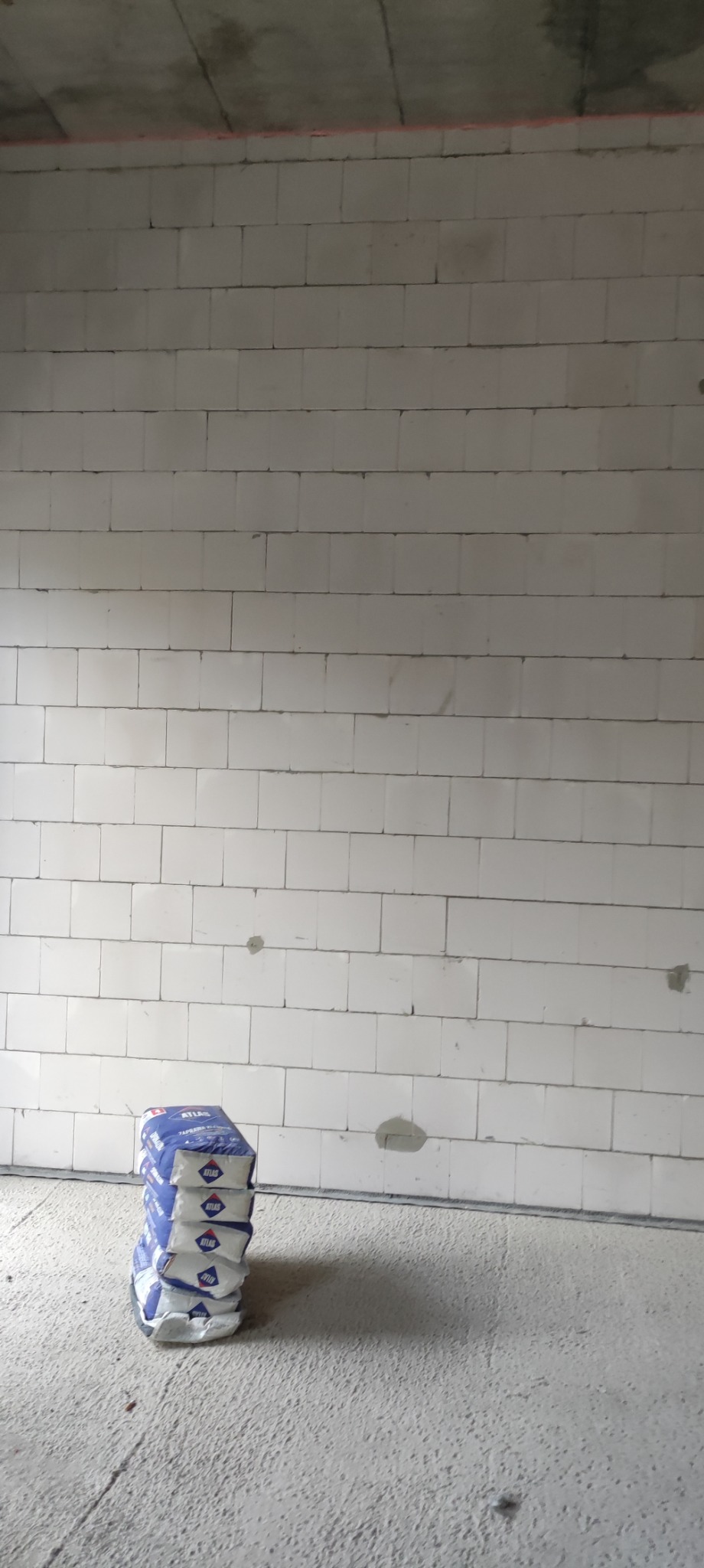 Świeżo wymurowana ściana z białych bloczków z betonu komórkowego, obok stos worków z zaprawą Atlas.