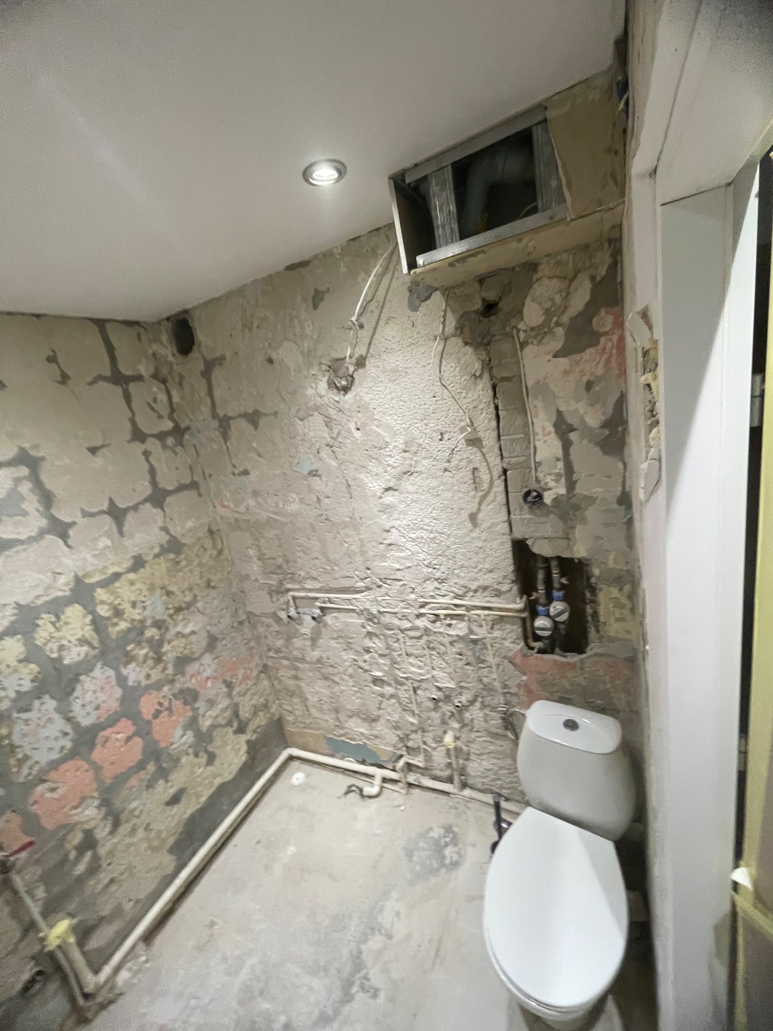 Łazienka w trakcie demontażu: odsłonięte instalacje, surowe ściany z resztkami farby, widoczny fragment toalety. Przygotowanie do remontu, widok z góry.