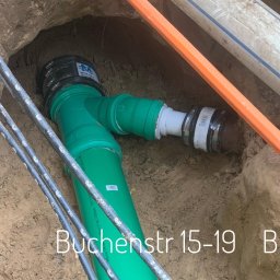 LEW SOLUTIONS Paweł Lewczuk - Zielona rura kanalizacyjna z łącznikiem w wykopie, widoczne kable i inne rury, ziemia wokół.